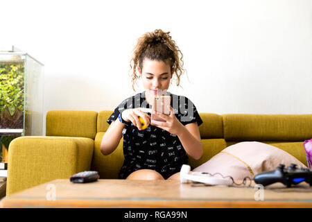 Portrait of girl sitting on the couch at home using smartphone Stock Photo