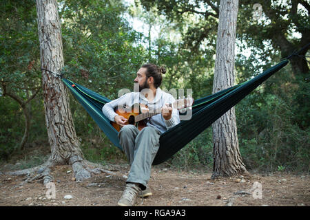 Man sitting in hammock playing guitar in the woods, partial view