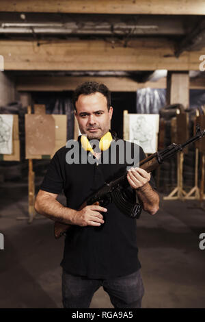 Portrait of man holding a rifle in an indoor shooting range Stock Photo