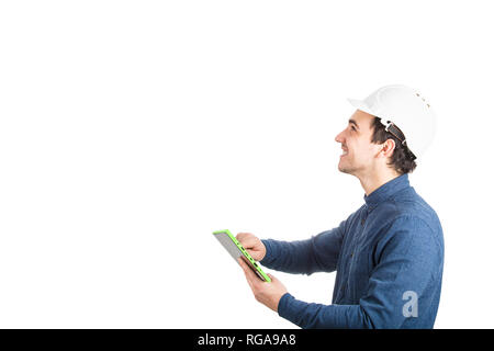 Side view of cheerful young man engineer wearing protective helmet using a tablet computer gadget looking up isolated over white background with copy  Stock Photo