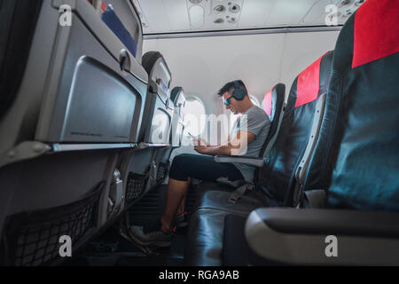 Man in airplane, using smartphone, headphones Stock Photo