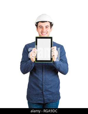 Creative cheerful young man engineer wearing protective helmet holding tablet computer showing blank screen to camera as for project plan presentation Stock Photo