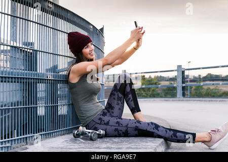 Young woman sitting on ground after dumbbell training, using smartphone Stock Photo