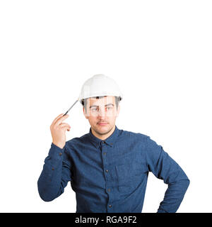 Pensive young man engineer wearing protective helmet thinking pointing pencil to head isolated over white background with copy space. Stock Photo