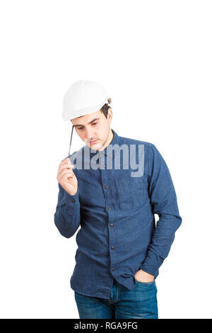 Thoughtful young man engineer wearing protective helmet thinking pointing pencil to head isolated over white background with copy space. Stock Photo