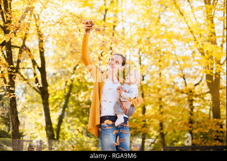 Mother and baby girl having fun with leaves in autumn Stock Photo