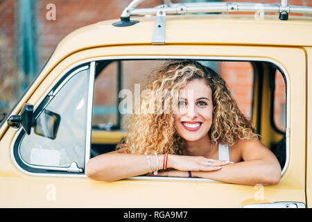 Portrait of happy blond woman looking out of window of classic car Stock Photo