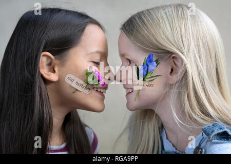 Profiles of two smiling girls with flower heads on their cheeks Stock Photo