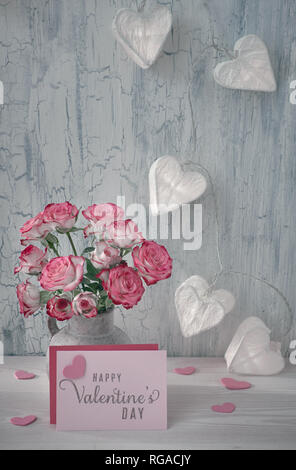 Valentines day still life with blank paper card, pink roses and garland lights in shape of paper hearts on rustic background Stock Photo