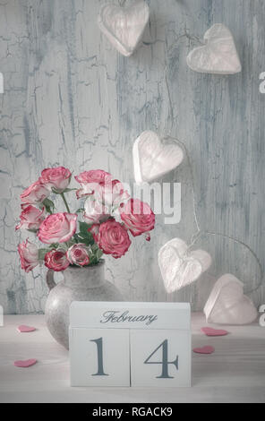 Valentines day still life with wooden calendar, pink roses and garland lights in shape of paper hearts on rustic background Stock Photo