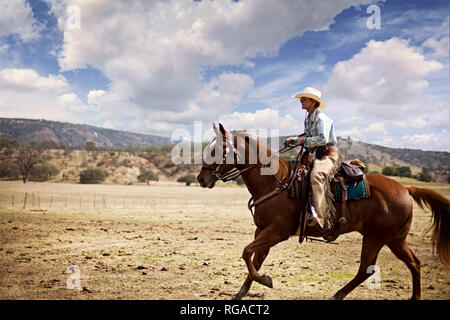 Woman wearing cowboy hat and spats riding horseback on a ranch Stock Photo