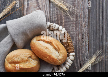 Bread buns in basket on rustic wood with wheat ears, top view Stock Photo