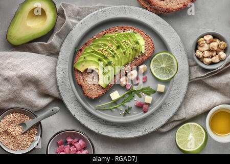 Green salad and sandwich with avocado with ingredients around, top view on grey stone background Stock Photo