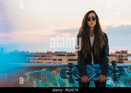 Portrait of cool young woman holding skateboard in the city Stock Photo