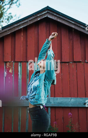 Portrait of a young woman stretching in front of a red wood hut Stock Photo