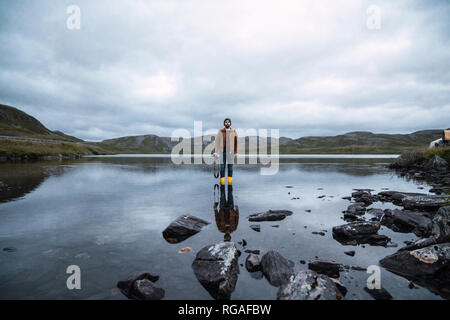 Young man standing ankle deep in water, holding camera Stock Photo