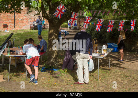 Union Flag bunting at a village fete with children and a man in a straw hat. Stock Photo