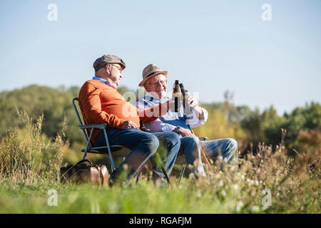 Two old friends sitting in the fields, drinking beer, talking about old times Stock Photo