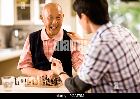 Adult son sitting in a kitchen while discussing his father's medication. Stock Photo