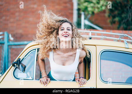 Portrait of blond woman leaning out of window of classic car tossing her hair Stock Photo