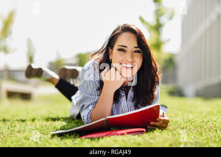 Portrait of smiling student lying on lawn with notebooks Stock Photo