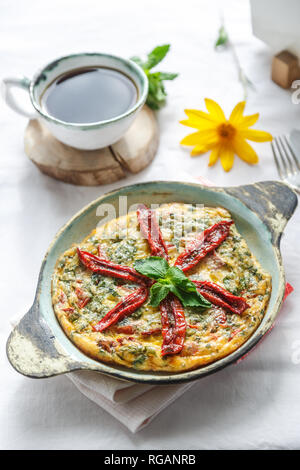 Traditional fritatta with dry tomatoes in a cast iron pan. White background, copy space Stock Photo