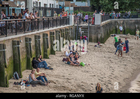 South Bank, Southwark, London, UK - August 6, 2014:  Sandy beach at the side of the River Thames on South Bank with people enjoying the late evening s