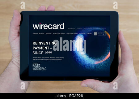 A man looks at the Wirecard website on his iPad tablet device, shot against a wooden table top background (Editorial use only) Stock Photo