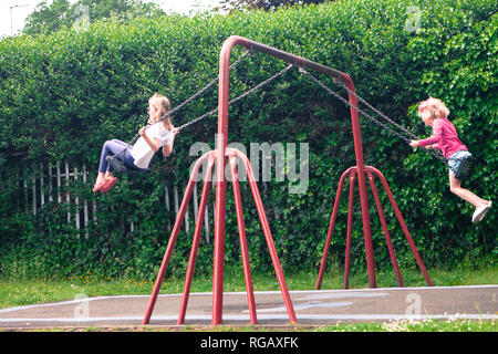 Two caucasion girls playing on swings in a park in a playground Stock Photo