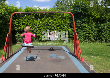 Two caucasion girls playing on swings in a park in a playground Stock Photo