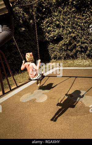 Two caucasion girls playing on swings in a park in a playground and shadows Stock Photo