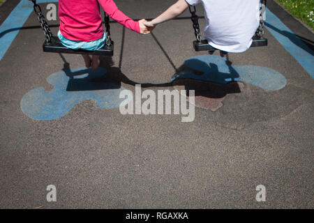 Two caucasion girls playing on swings in a park in a playground Stock Photo