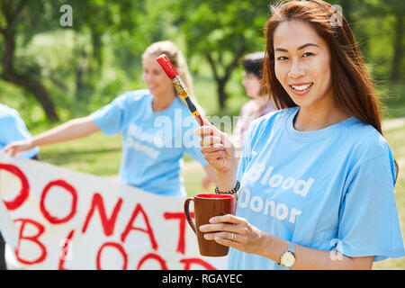 Young volunteer volunteer with paint and brush in front of the Donate Blood poster Stock Photo