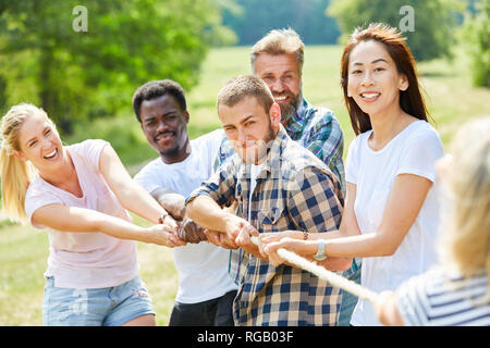 Determined team pulling rope in tug-of-war at park, Stock Photo