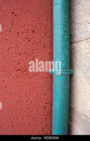 green painted down pipe in the corner of a pink and white wall join creating an abstract image Stock Photo