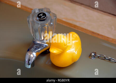 Yellow plastic duck beside hot tap on avocado coloured bath. Stock Photo