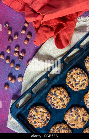 Avena cookies with hazelnuts and chocolate chips on a baking sheet and some hazelnuts and cloths Stock Photo