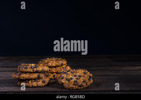 Some avena cookies with hazelnuts and chocolate chips on an old wooden table and dark background Stock Photo