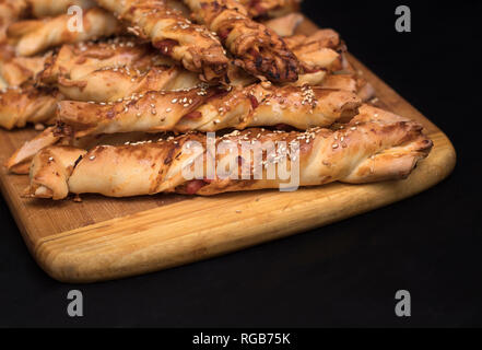 twisted cheese bread sticks with ham and sesame seeds on a wooden board on a black background Stock Photo