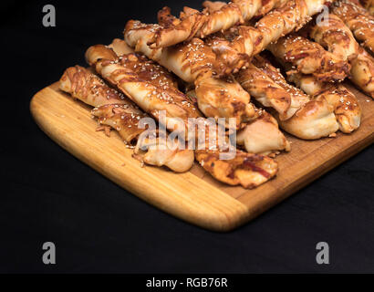 twisted cheese bread sticks with ham and sesame seeds on a wooden board on a black background Stock Photo