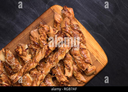 twisted cheese bread sticks with ham and sesame seeds on a wooden board on a black background Stock Photo