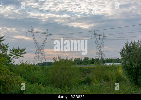 Twin power line towers in a large open green field on a cloudy day during sunset. Stock Photo