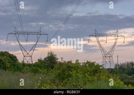 Twin power line towers in a large open field on a cloudy day during sunset. Stock Photo