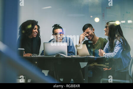 Group of happy young students in university library sitting at a table with their laptop and smiling. Multi-ethnic college students smiling while stud Stock Photo