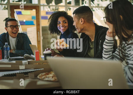 Group of students eating pizza at college canteen. Multi-ethnic men and women students eating at university campus cafe. Stock Photo