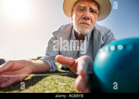 Close up of a senior man lying on ground and measuring the distance between boules using a measuring device. Senior man checking the distance between Stock Photo
