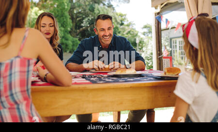 Couple with their children dining in their backyard. Man and woman eating snacks with their kids at the dining table. Stock Photo