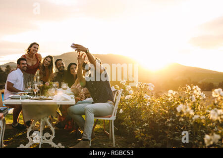 Man with friends taking selfie using his smart phone. Group selfie at outdoor dinner party. Stock Photo