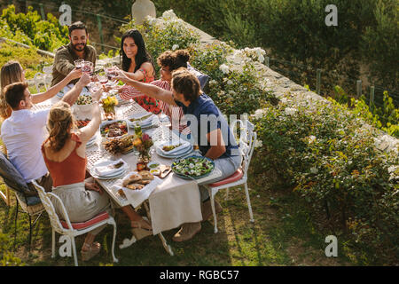Group of men and women sitting at table and toasting drinks. Group of friends toasting wine at dinner party. Stock Photo