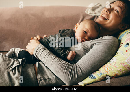 Smiling mother lying on couch with her baby sleeping on her chest. Happy mother relaxing at home with her child sleeping on her Stock Photo Alamy